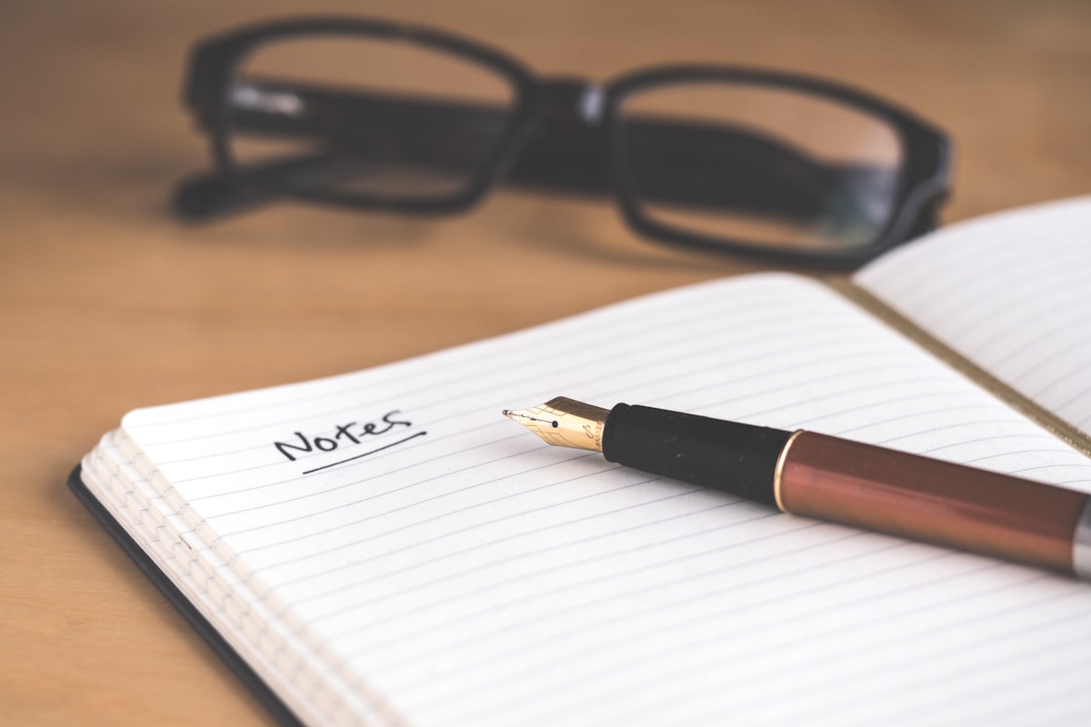 An open notebook with a pen on a wooden desk in soft daylight